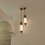 Zerith LED alabaster tube pendant lights with fluted brushed brass collars and domed end caps, shown illuminated on brass ceiling rods against a plaster archway wall.