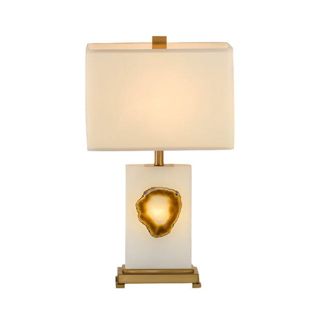 The Selune 1 Light Sculpted Core Alabaster Table Lamp features a modern alabaster base with a brushed brass geode-like accent, gold detailing, and a soft white rectangular shade.