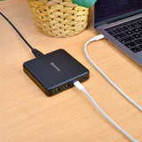 Mercury 65W GaN charger in matt black on a wooden desk, powering a laptop via USB-C with a second white cable plugged into the C2 port.