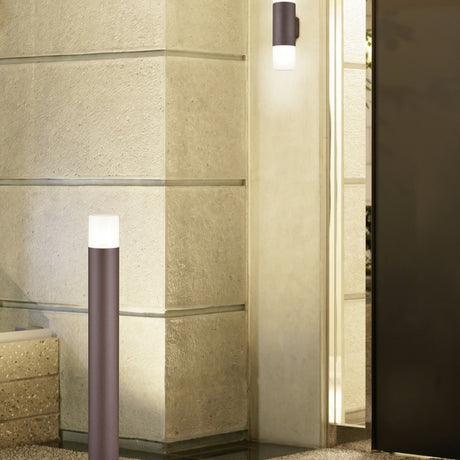 Hoosic 80cm outdoor lamp post in rust, aluminium pole with frosted cylinder shade, shown beside a matching wall light on a stone wall at an entrance.