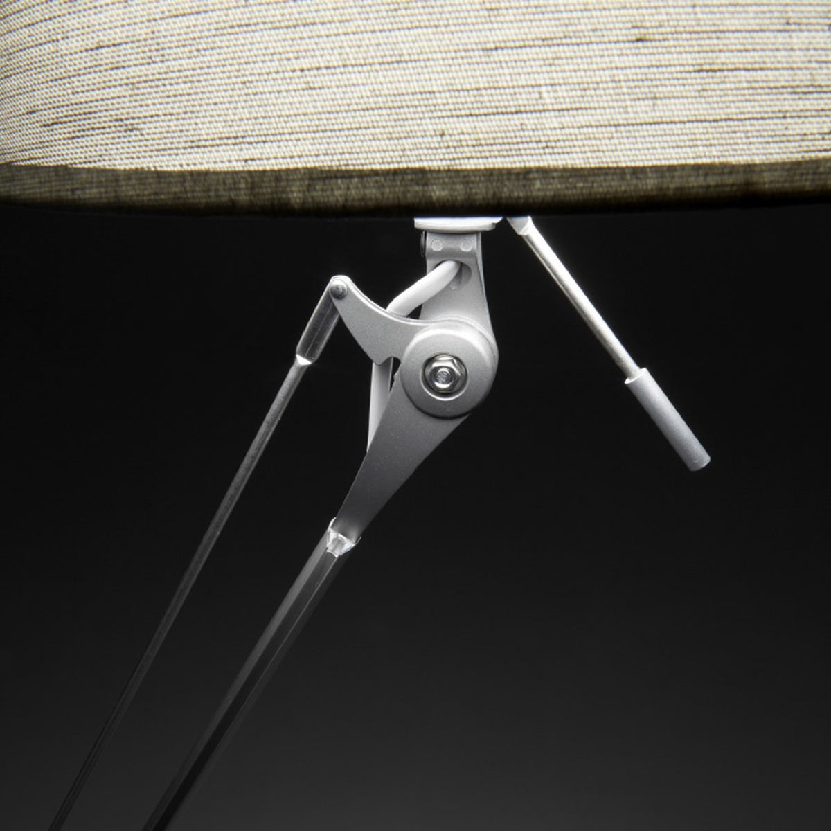 Close-up of the Hesmorne floor lamp's articulated silver aluminium arm and joints beneath a cream woven fabric drum shade, set against a dark background.