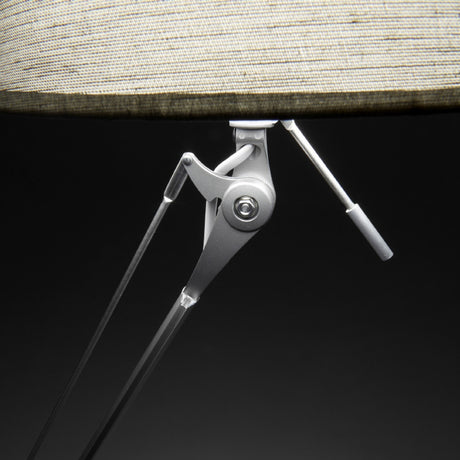 Close-up of the Hesmorne floor lamp's articulated silver aluminium arm and joints beneath a cream woven fabric drum shade, set against a dark background.