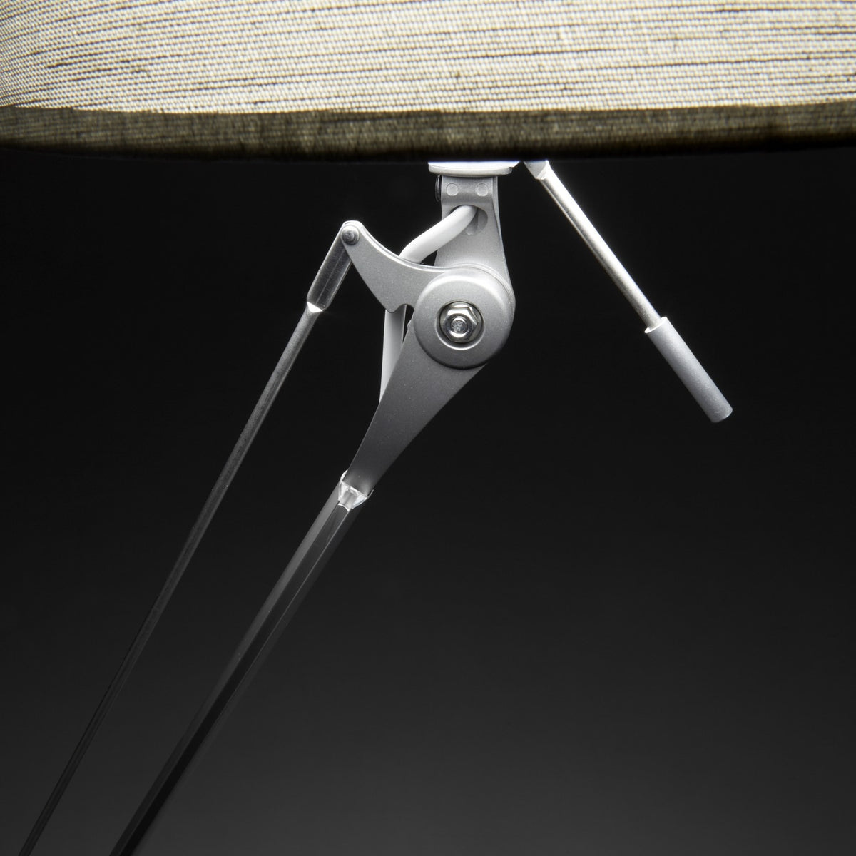 Close-up of the Hesmorne floor lamp's articulated silver aluminium joint and adjustable arm beneath a cream woven fabric drum shade, set against a dark background.