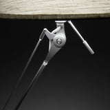 Close-up of the Hesmorne floor lamp's articulated silver aluminium joint and adjustable arm beneath a cream woven fabric drum shade, set against a dark background.