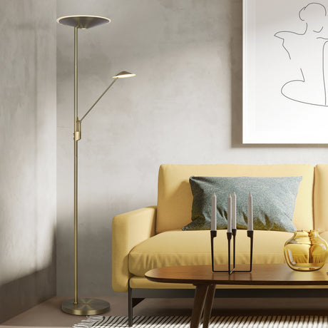 Brantford 2 Light LED Floor Lamp in antique brass with an upward-facing main head and jointed reading arm, shown beside a yellow sofa in a living room setting.