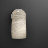 Paros Alabaster Wall Light in White, a curved alabaster shade with soft grey veining on a white iron backplate and arm, shown against a dark background.