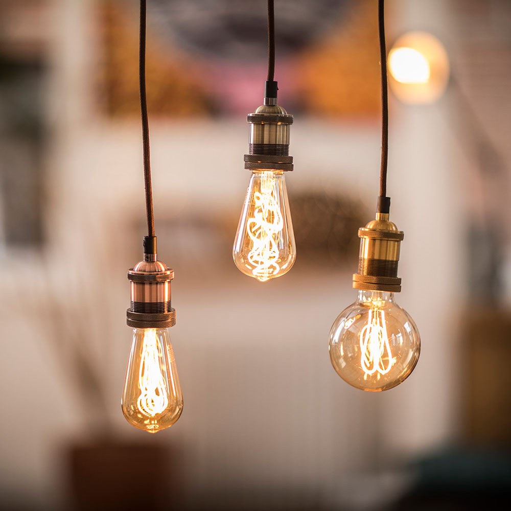 LYYT ES Pendant Set by AVSL shown as three antique brass E27 holders with braided cords, suspending vintage filament bulbs in a warm-lit interior.