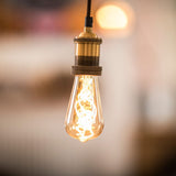 LYYT ES pendant set by AVSL in antique gold, single E27 lamp holder with knurled detailing on braided cable, shown lit with a vintage filament bulb.