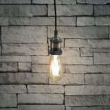 LYYT ES pendant set by AVSL in antique copper, lit E27 filament bulb hanging from braided cable against a white-washed brick wall.