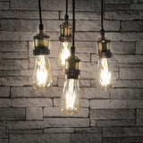 LYYT ES Quad Pendant Set in antique brass with four E27 lamp holders on braided cables, fitted with Edison-style filament bulbs against a grey brick wall.