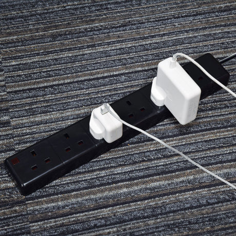 AVSL Mercury 6 Gang 13A trailing socket in black with two white Apple plug adapters connected, shown on a striped grey carpet floor.