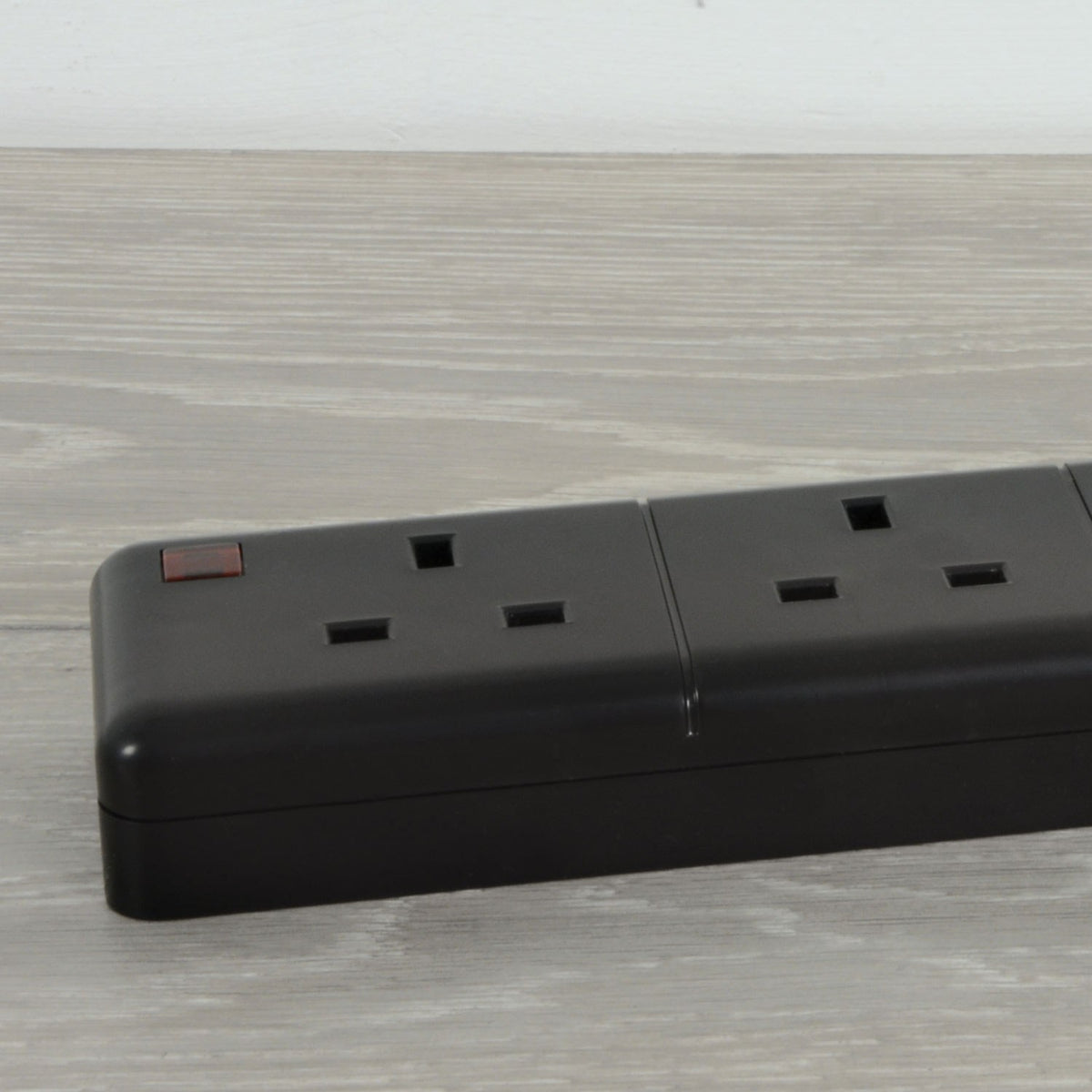 Close-up of the AVSL Mercury 6 Gang 13A trailing socket in black thermoplastic, showing UK 3-pin outlets and a red neon indicator on a light wood surface.