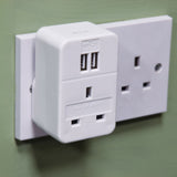 AVSL Mercury 1 Way Mains Adaptor in white plastic with dual USB-A ports and a 13A pass-through socket, plugged into a UK wall socket on a green wall.
