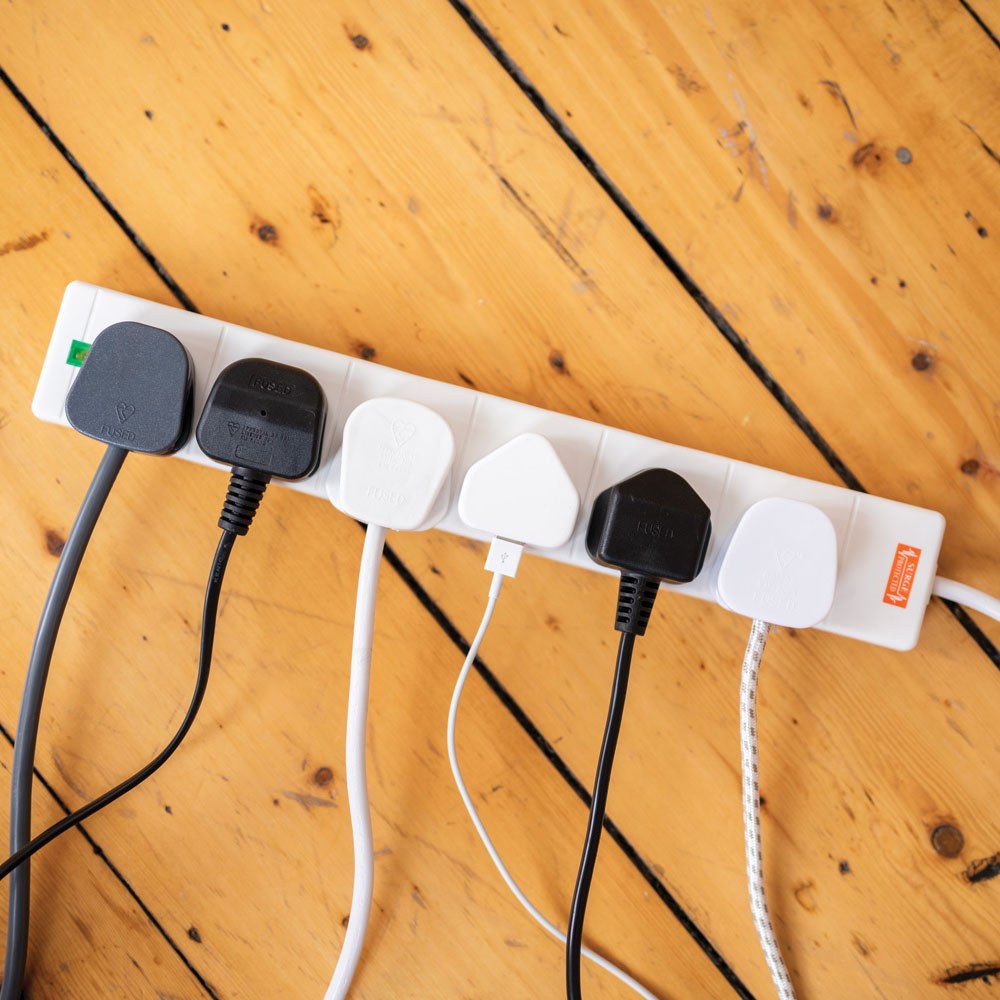 AVSL Mercury 6 Gang Extension Lead in white with all six UK sockets in use by black and white plugs and a USB adapter, shown on a wooden floor.