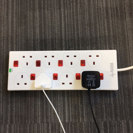 Mercury 8 gang extension lead in white with red neon switches on each socket, surge protected label, and two plugs connected, on grey carpet.