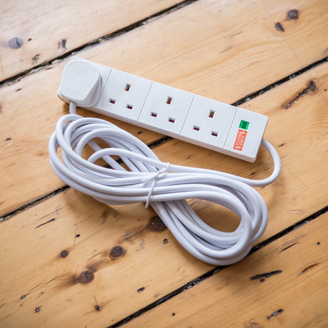 Mercury 4 gang extension lead by AVSL with white housing, three visible UK sockets, orange surge protected label and coiled 5m cable on wooden floorboards.