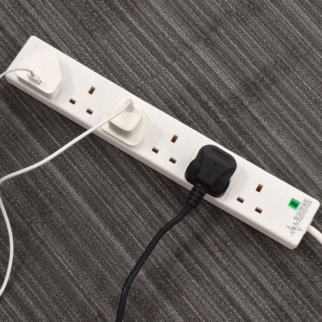 AVSL Mercury 6 gang extension lead in white with surge protection, three UK plugs connected and green neon indicator, shown on grey carpet.
