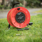 Mercury 25m 4 gang cable reel in orange with black steel frame, carry handle and 13A fused plug, shown on grass outdoors.