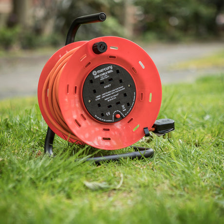 Mercury 25m 4 gang cable reel in orange with black steel frame, carry handle and 13A fused plug, shown on grass outdoors.