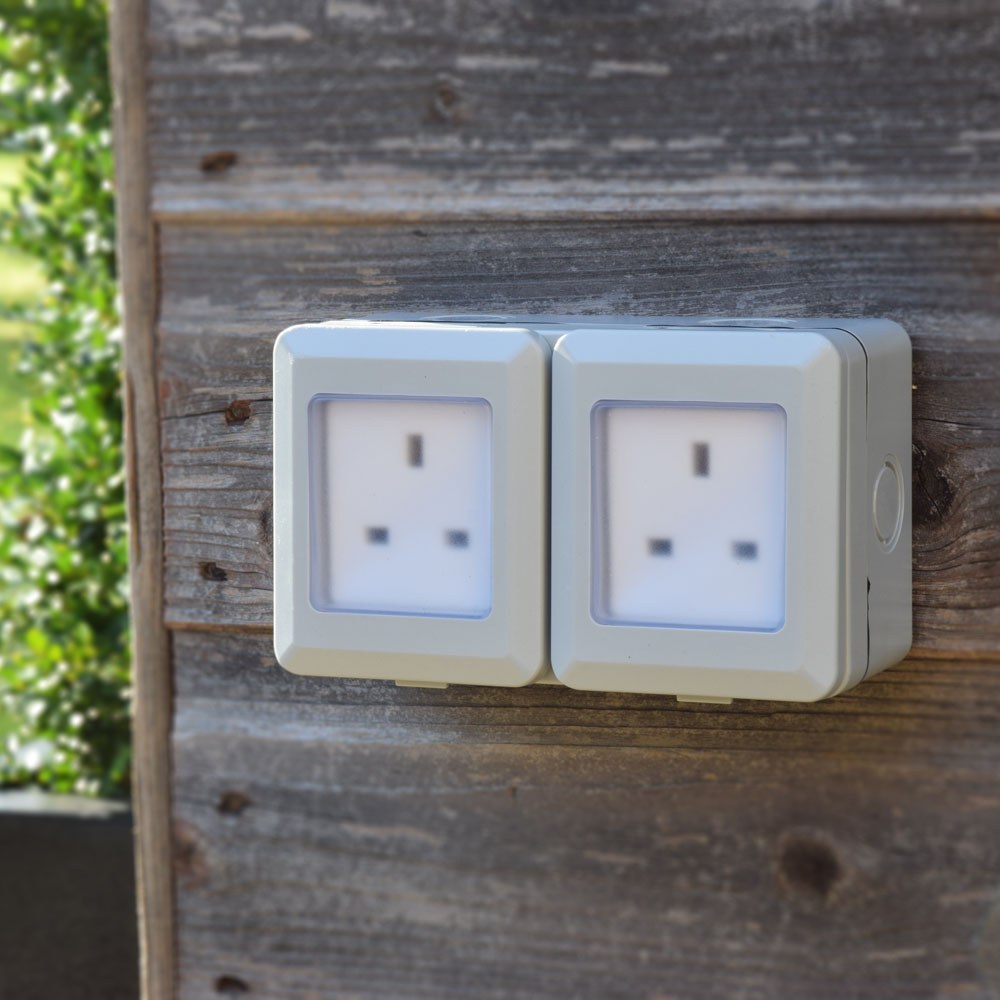 AVSL Mercury IP55 2 gang weatherproof socket in white with transparent hinged covers over twin UK outlets, surface-mounted on a weathered timber wall.