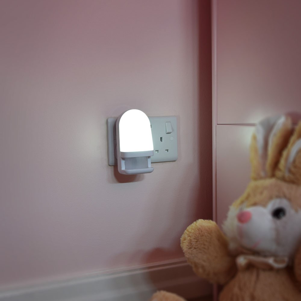 LYYT LED night light with PIR motion sensor plugged into a socket on a pink nursery wall, illuminated beside a plush bunny toy.