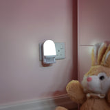 LYYT LED night light with PIR motion sensor plugged into a socket on a pink nursery wall, illuminated beside a plush bunny toy.