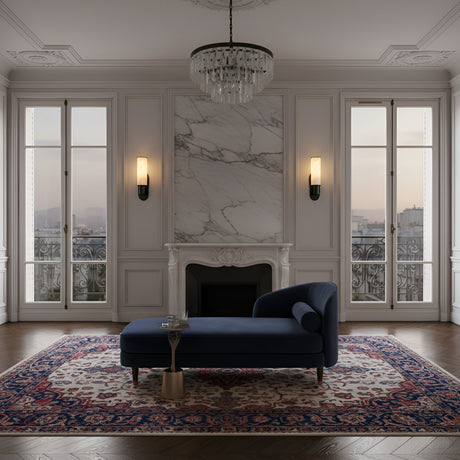 Elegant living room with a marble fireplace, chandelier, Lumara 1 Light Tube Alabaster Wall Light in soft white & matte black, two tall windows, dark blue chaise lounge, side table, patterned rug on wood floors, and cityscape views.