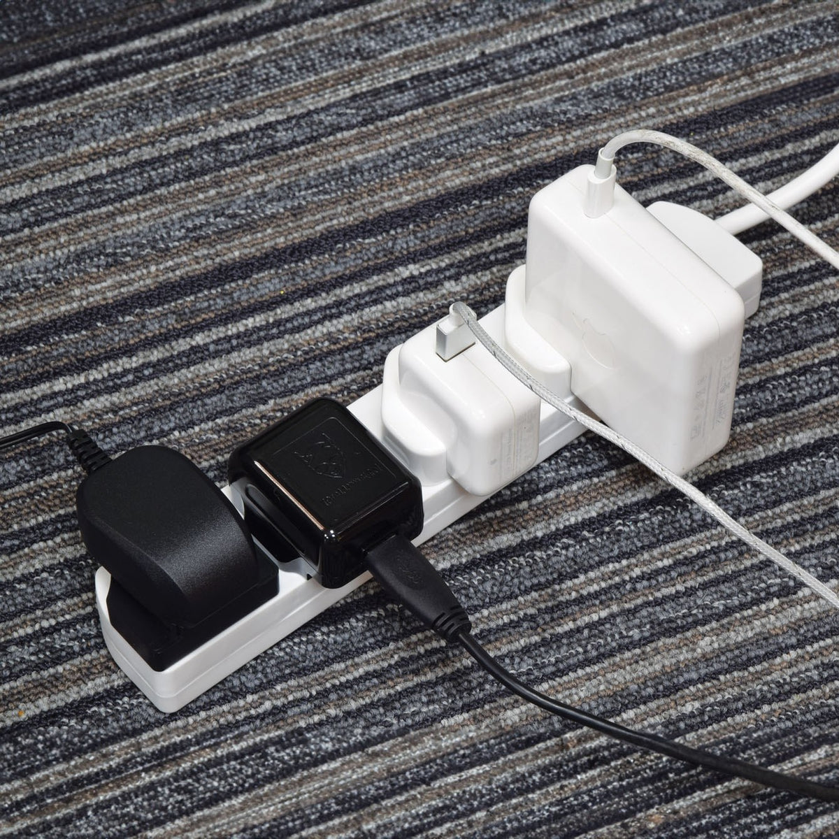 AVSL Mercury 4 gang extension lead in white ABS with three UK chargers plugged in, resting on a grey striped carpet.