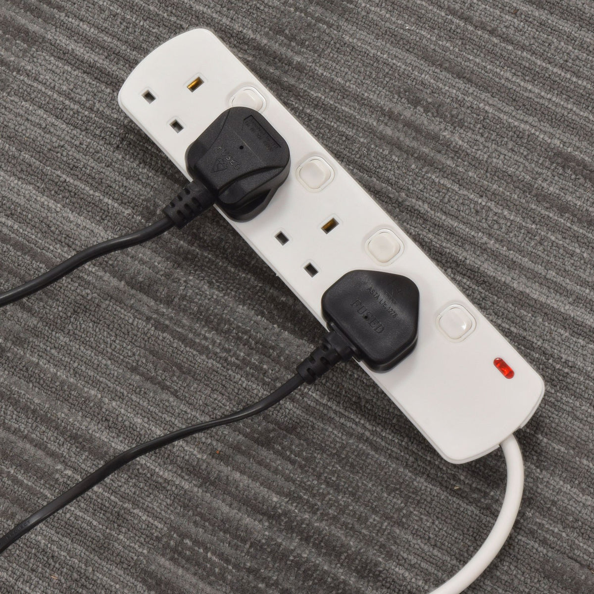 AVSL Mercury 4 gang switched extension lead in white with two black UK plugs connected, resting on a grey carpeted surface with red indicator lit.