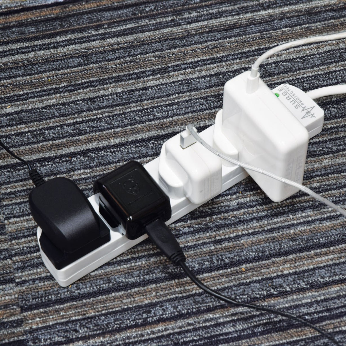 AVSL Mercury 4 gang surge protected extension lead in white with four UK sockets in use, chargers plugged in, shown on a grey striped carpet.