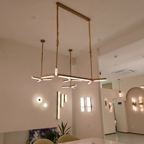 Elvaris LED Small Vertical Alabaster Wall Light in Brushed Brass, shown illuminated among pendant and wall lighting in a modern showroom setting.