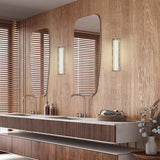 Kalvenne LED Glass Wall Light in satin bronze with ribbed glass shade, shown illuminated beside a mirror in a wood-panelled bathroom vanity setting.