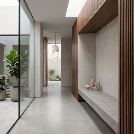 Modern minimalist hallway with concrete floor, wooden slat wall, built-in bench, abstract vases, large potted plant, glass wall, and a Half Moon LED Pendant Light - Silver, leading to an outdoor courtyard filled with greenery.