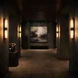 A dimly lit modern hallway with dark walls, a bench, and a cloud-themed painting at the end features Caldera LED Small Floating-Band Alabaster Wall Lights (Matte Black & Soft White) and a geometric sculpture, creating a moody, sophisticated vibe.