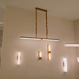Elvaris LED Linear Alabaster Chandelier in brushed brass, shown suspended from a ceiling plate on twisted cords above a wall with matching alabaster wall lights.