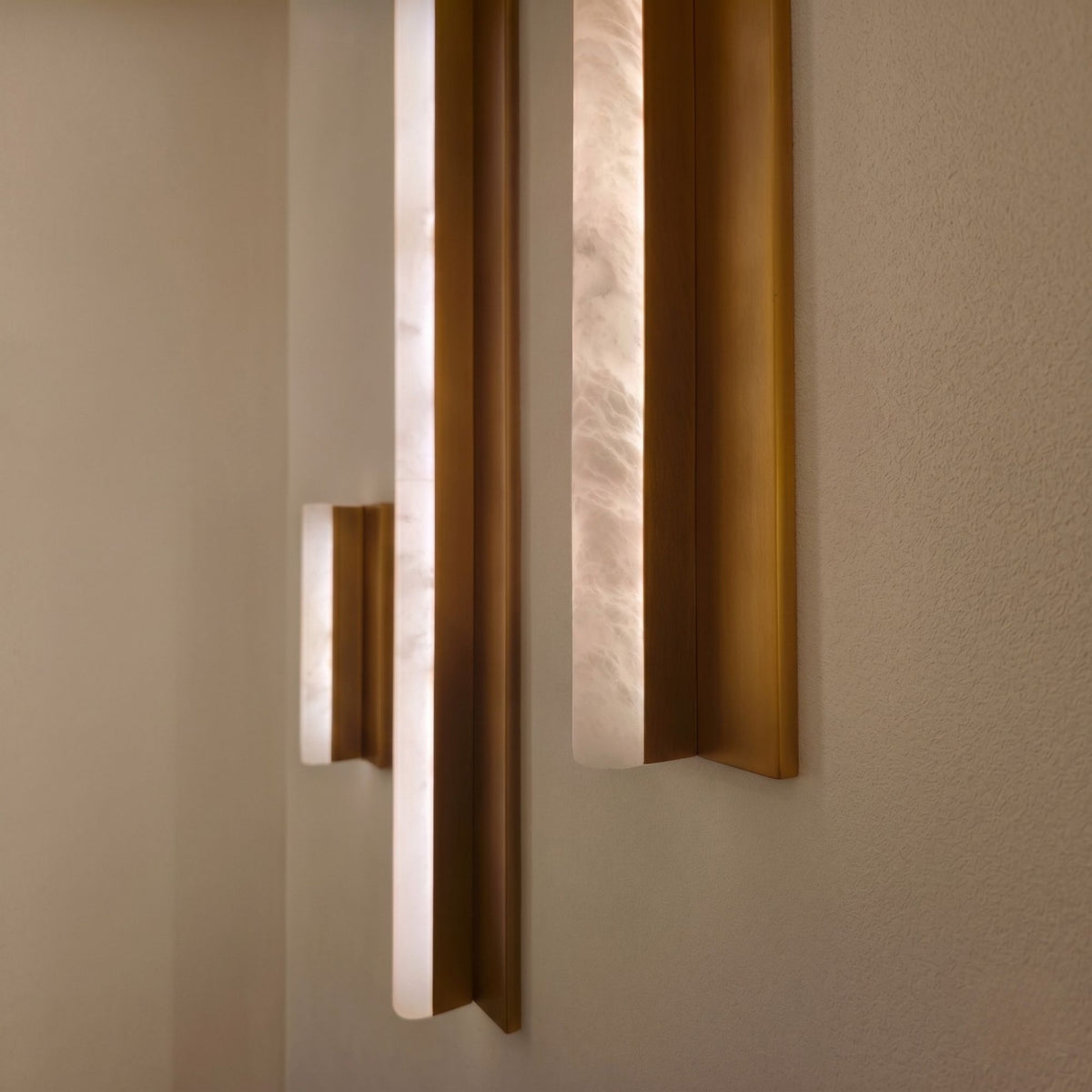 Elvaris LED Vertical Alabaster Wall Light Medium in brushed brass, showing glowing alabaster panels within angled brass fins mounted on a light wall.