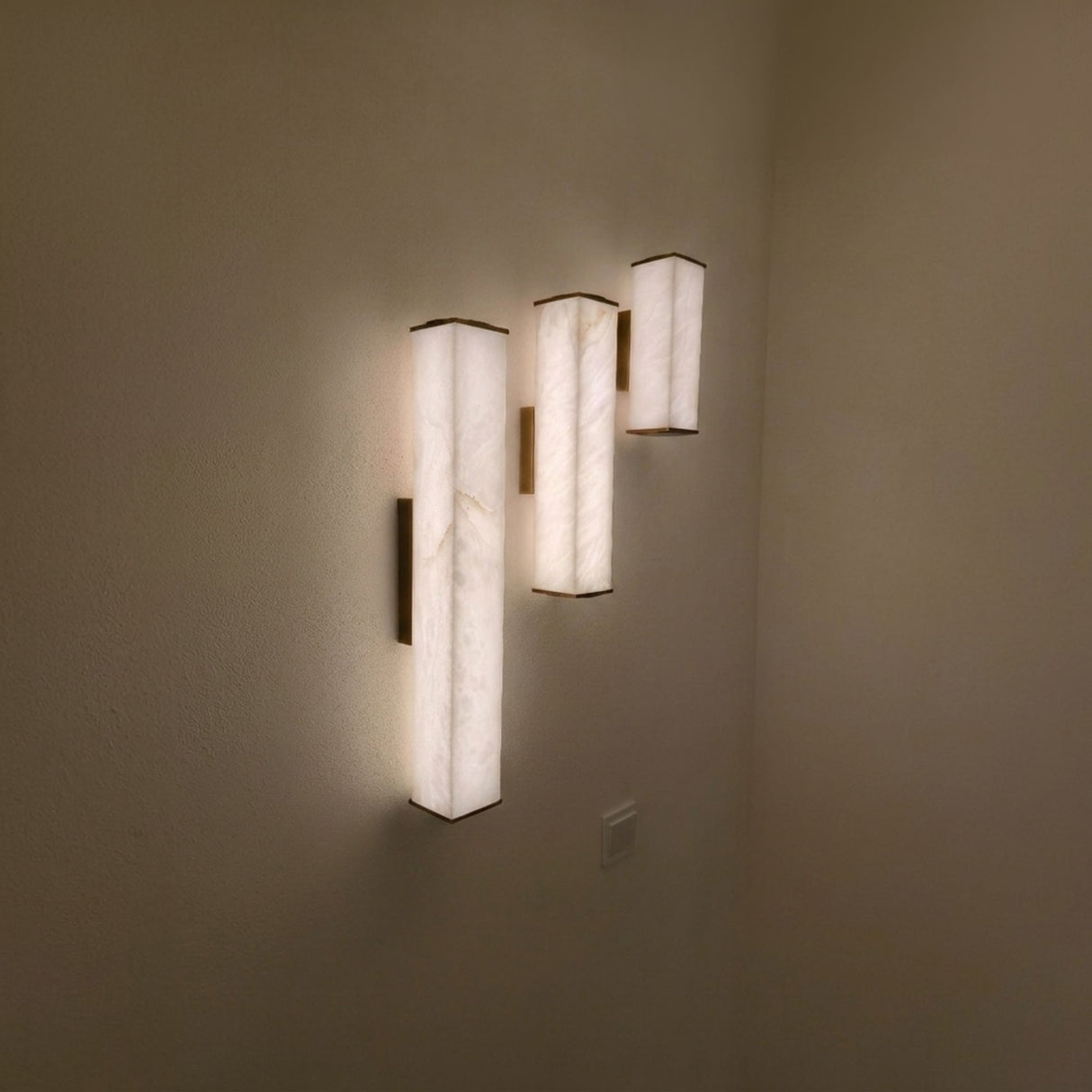Valmere LED Linear Alabaster Wall Light in soft white and brass, three vertical fixtures glowing warm white on a wall in a dimly lit room.