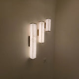 Valmere LED Linear Alabaster Wall Light in soft white and brass, three vertical fixtures glowing warm white on a wall in a dimly lit room.