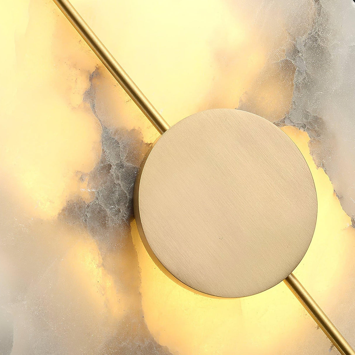 Close-up of the Elaris LED Round Alabaster Wall Light in soft white and brass, featuring a round brushed gold center and slim rod, mounted on a glowing marbled surface—an elegant choice for contemporary interiors.