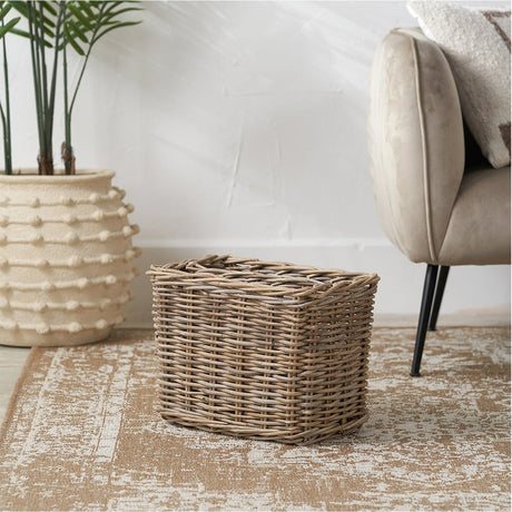 Tobs Grey Kubu Rattan Magazine Basket, 30cm tall, rectangular woven storage basket shown on a rug beside a sofa and potted plant in a living room setting.