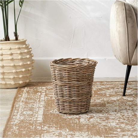 Tobs grey Kubu rattan waste paper bin, 33cm woven storage box shown tapered and open-topped on a rug beside a plant pot and armchair.