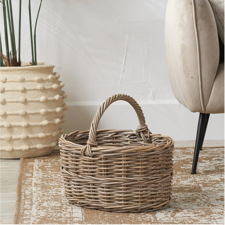 Tobs Grey Kubu Rattan Straight Sided Shopping Basket, 40cm, with woven arched handle, shown on a rug beside a plant pot and armchair.