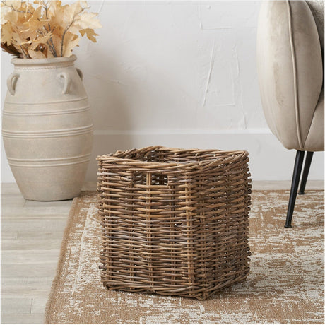 Tobs Grey Kubu Rattan Storage Basket, 35cm square woven design with cut-out handles, shown on a rug beside a stone vase and upholstered chair.
