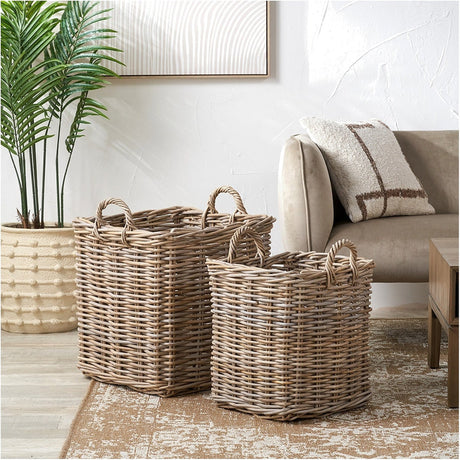 Tobs Set of 2 Grey Rattan Log Baskets, 59cm, with woven handles, shown beside a sofa on a rug in a living room setting.