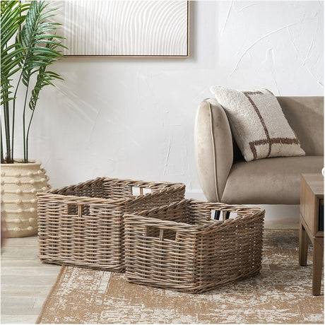 Tobs Set of 2 Grey Kubu Rattan Rectangular Storage Baskets with cut-out handles, shown in a living room beside a sofa, cushion, and potted plant.