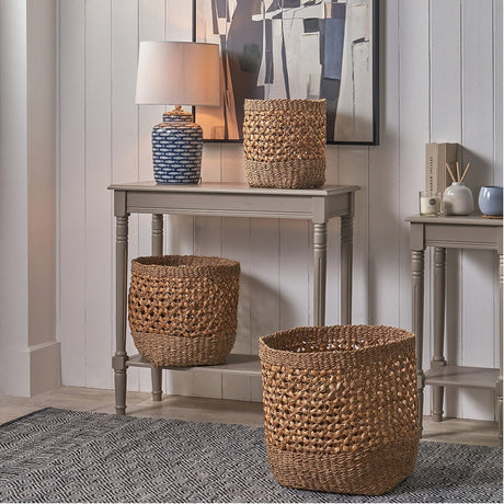 Set of 3 natural seagrass and water hyacinth tall baskets in graduated sizes, styled on and beside a grey console table in a living room setting.
