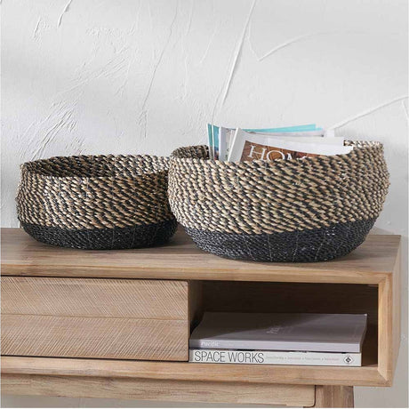Set of 2 round seagrass storage baskets, 38cm, with natural woven sides and black woven base, shown on a wooden console table holding magazines.