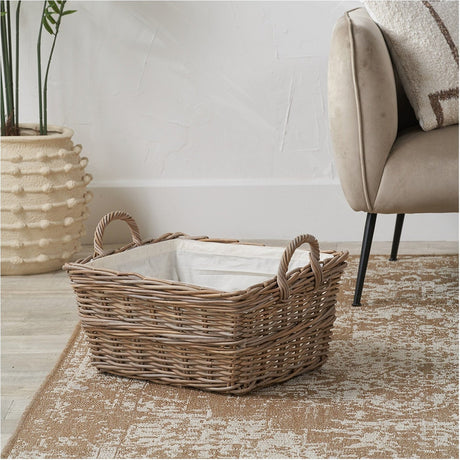 Grey Kubu Rectangular Handled Laundry Basket, 30cm rattan weave with white fabric lining and woven side handles, shown on a rug beside an armchair.