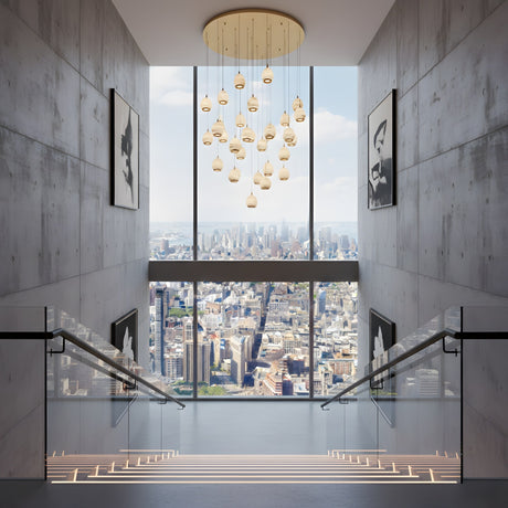 Niori Aurevia 31 Light LED alabaster chandelier in brushed brass, cascading pebble-shaped drops above a concrete stairwell with city skyline views.