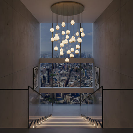 Niori Aurevia 31 Light LED alabaster chandelier in brushed brass, cascading pebble-shaped drops above a staircase with city skyline views.